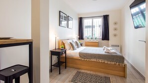 A bedroom with a bed, bedside tables, a window with curtains, a wall-mounted TV, and a small plant. - Magnificent Studio - 2P - Moulin Rouge (Paris)