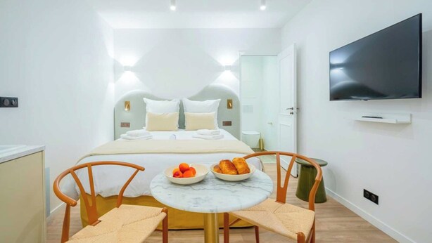 Habitación de hotel con cama, televisión, una mesita con fruta y dos sillas.