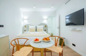 A hotel room with a bed, a TV, a small table with fruit, and two chairs. - Cosy Studio - Hyper Centre St Tropez (Saint-Tropez)