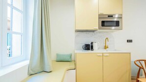 Una cocina compacta con horno empotrado, un lavamanos con grifo dorado y una pequeña zona de estar con cojín.