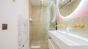 Un baño moderno con ducha envuelta en vidrio, tocador blanco con detalles dorados y un espejo grande con luz circular.