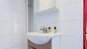A bathroom with white tiled walls, a white sink with a wooden vanity, and a red curtain. - Beautiful Studio 1 - Edouard Vaillant (Pantin)