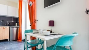 A compact kitchen with a white countertop, two teal chairs, a white table, and a purple lamp. - Beautiful Studio 1 - Edouard Vaillant (Pantin)