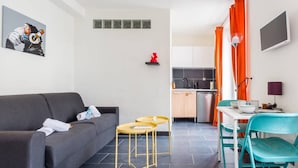 A compact living space with a grey sofa, two small round tables, a kitchen area with a white countertop, and orange curtains. - Beautiful Studio 1 - Edouard Vaillant (Pantin)