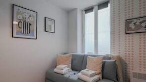 Een moderne woonkamer met een grijze bank, twee decoratieve kussens en een ingelijste afbeelding aan de muur.