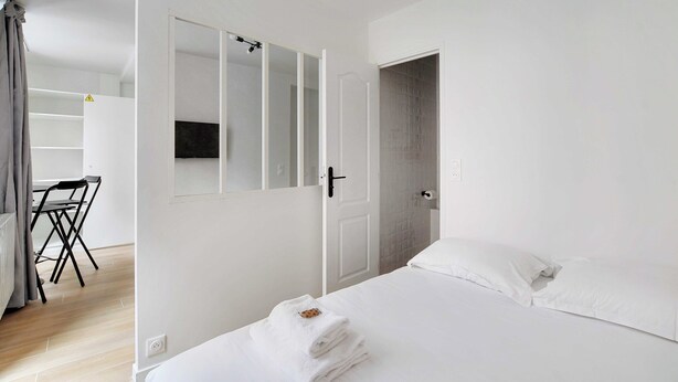 A minimalist bedroom with a bed, a desk, and a chair. - Newly Renovated Appartement Hotel Residence (Paris)