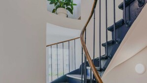 A spiral staircase with black railings and wooden handrails, leading to a balcony with a potted plant. - Newly Renovated Appartement Hotel Residence (Paris)