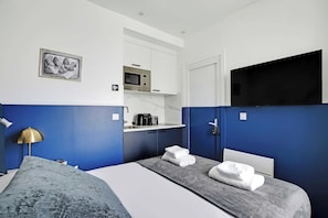 A hotel room with a bed, a TV, a microwave, a sink, and a blue accent wall. - Serene Cocoon for 2P With AC - Near Montmartre (Paris)