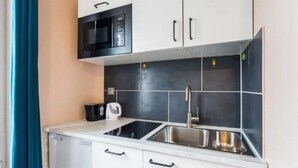 Une cuisine compacte avec des meubles blancs, un micro-ondes noir, un évier en acier inoxydable et une bouilloire.