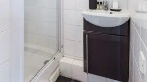 Une salle de bain moderne avec une douche à l’italienne en verre, un lavabo blanc avec des meubles de rangement de couleur foncée, et un miroir au-dessus du lavabo.