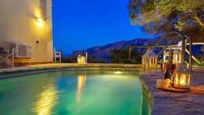 A swimming pool with a view of mountains at dusk, surrounded by outdoor seating and decorative lanterns. - Villa Rosa dei Venti, Scopello (CASTELLAMMARE DEL GOLFO)