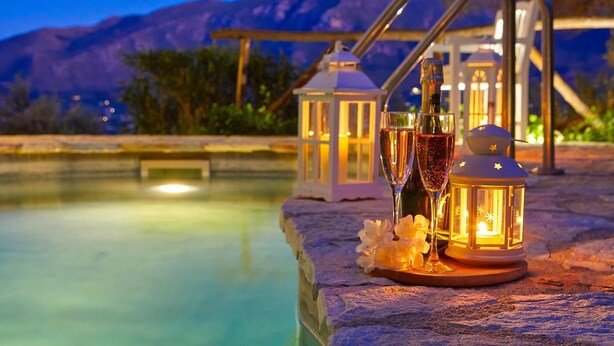 A poolside setting with a lantern, two champagne flutes, and a bottle, surrounded by a stone ledge and a white lantern structure. - Villa Rosa dei Venti, Scopello (CASTELLAMMARE DEL GOLFO)