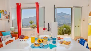 A dining area with a table set for breakfast, including croissants, fruit, and a pitcher of juice. - Villa Rosa dei Venti, Scopello (CASTELLAMMARE DEL GOLFO)