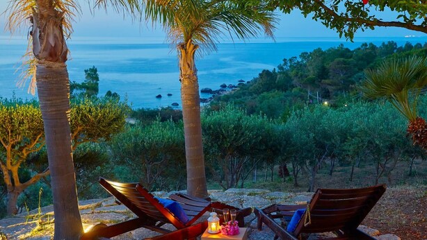 A sunset view with two wooden lounge chairs and a small table with a lantern and flowers. - Villa Ginestra, Scopello (CASTELLAMMARE DEL GOLFO)