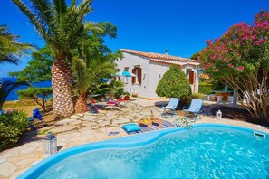 A poolside area with lounge chairs, a small pool, and a white building with a tiled roof. - Villa Ginestra, Scopello (CASTELLAMMARE DEL GOLFO)