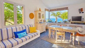 A modern living room with a sofa, dining table, and kitchen area. - Villa Ginestra, Scopello (CASTELLAMMARE DEL GOLFO)
