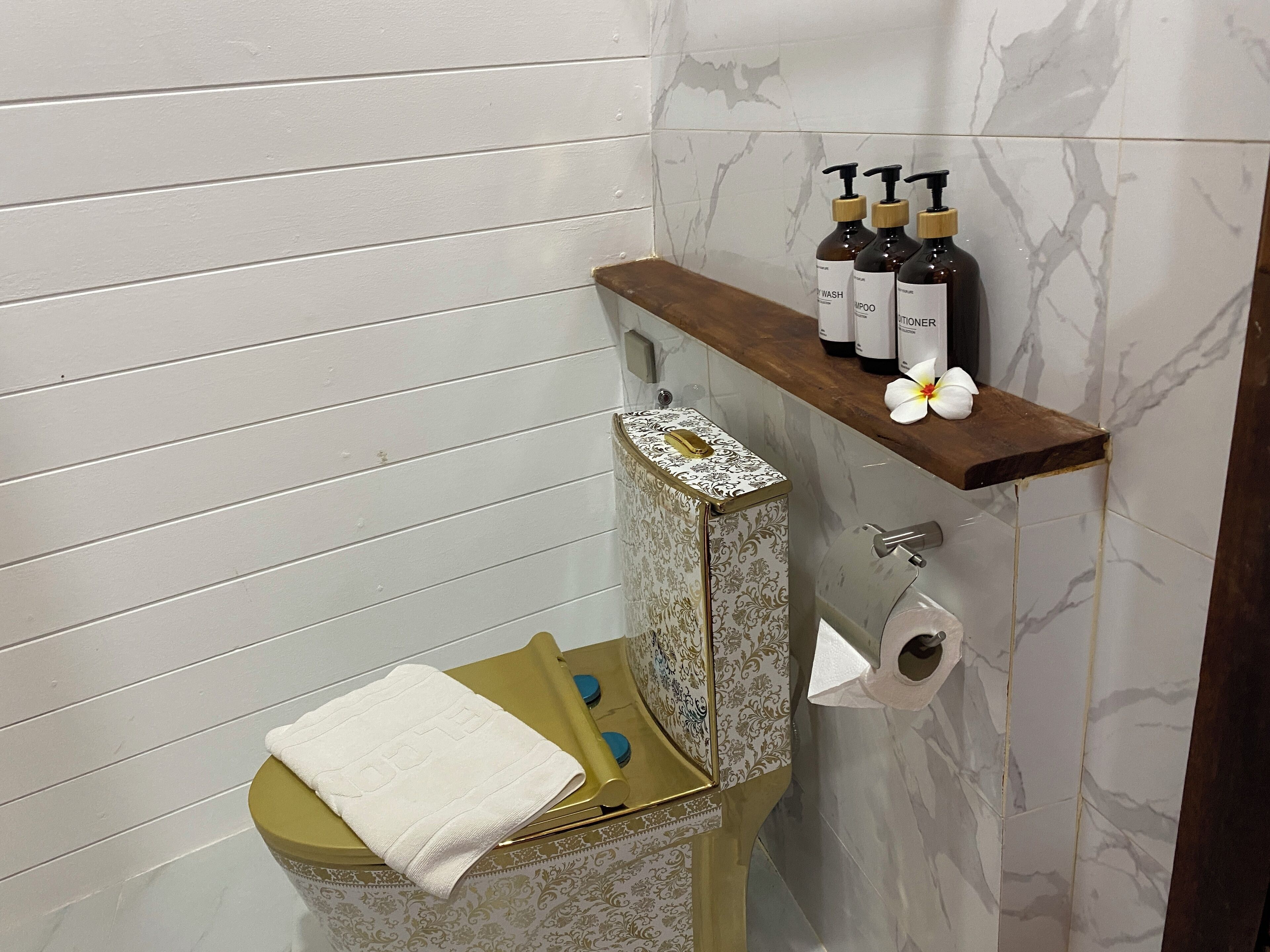 A bathroom with a toilet, a shelf with toiletries, and a decorative towel.