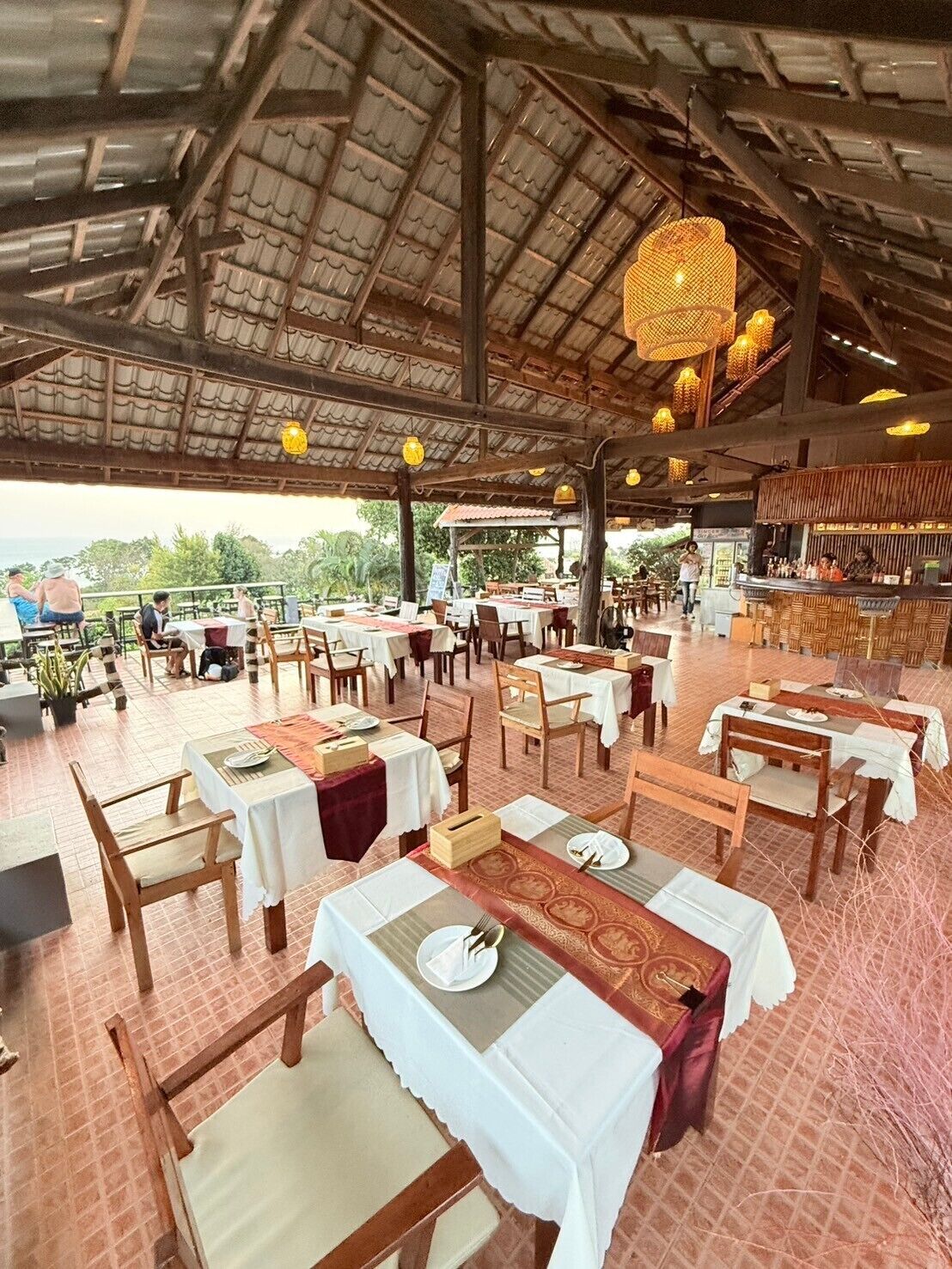 An outdoor restaurant with multiple tables and chairs, a bar area, and a covered seating area.