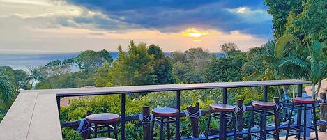 A terrace with outdoor seating and a scenic view of the ocean and hills.