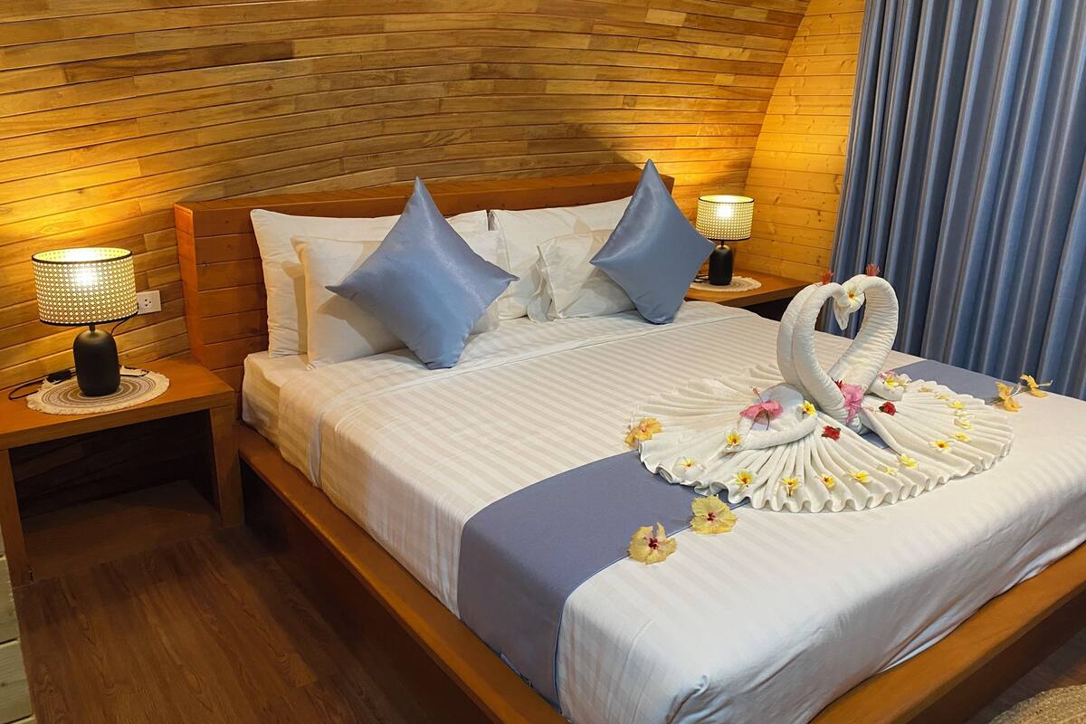 Una cama bien hecha con una decoración de toalla con forma de cisne, dos almohadas azules y dos lámparas de noche.