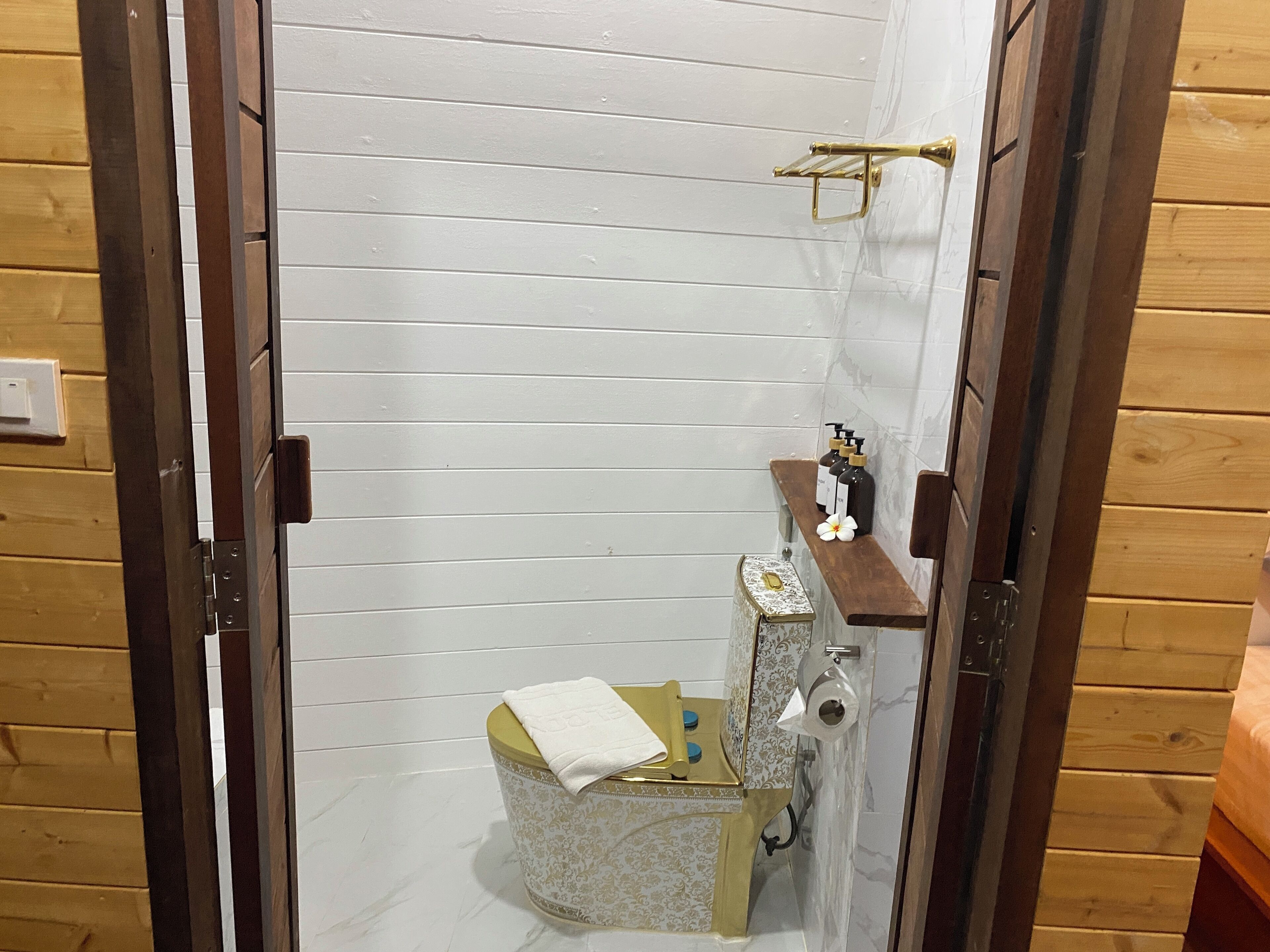 Un baño pequeño y funcional con suelo de madera, inodoro, lavamanos con toalla y zona de ducha.