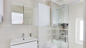 A modern bathroom with a white sink, mirror, and glass shower enclosure. - Stunning Studio for 2 People - Sentier (Paris)
