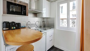 A compact kitchen with a microwave, kettle, and coffee maker on the counter, a stainless steel sink, and a window with a balcony view. - Stunning Studio for 2 People - Sentier (Paris)