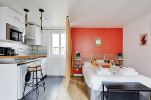 A modern hotel room with a kitchen area, a bed with white linens, and a red accent wall. - Stunning Studio for 2 People - Sentier (Paris)