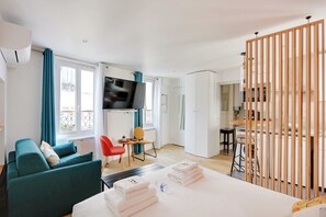 A modern hotel room with a sofa, a dining area, a TV, and a kitchen in the background. - Stunning Studio for 2 People - Sentier (Paris)