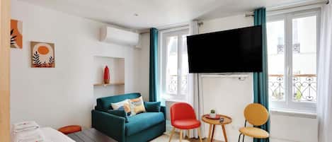 Une chambre d’hôtel moderne avec un canapé, un fauteuil rouge, une petite table et un téléviseur fixé au mur.