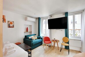 A modern hotel room with a sofa, a red chair, a small table, and a TV mounted on the wall. - Stunning Studio for 2 People - Sentier (Paris)