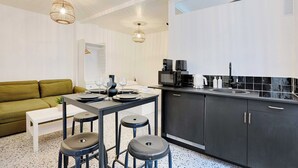 A modern kitchen with a dining area, including a table set for four, a sofa, and bar stools. - Cosy Studio - 2P - Place de la Bastille (Paris)