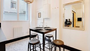 A dining area with a table set for four, a large mirror, and a window with blinds. - Cosy Studio - 2P - Place de la Bastille (Paris)