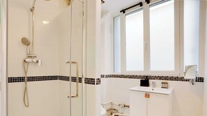 A bathroom with a glass-enclosed shower, a white sink with a mirror above it, and a tiled backsplash. - Cosy Studio - 2P - Place de la Bastille (Paris)