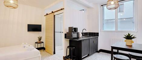 Una cocina moderna con encimera negra, un fregadero y un microondas. Hay un televisor montado en la pared, una ventana con vistas y una puerta que da a otra habitación.