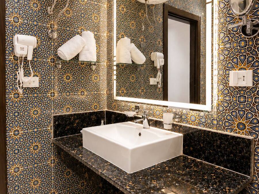 Un baño con lavamanos blanco, un espejo grande, ganchos para toallas y un revestimiento de pared con diseño de baldosas.