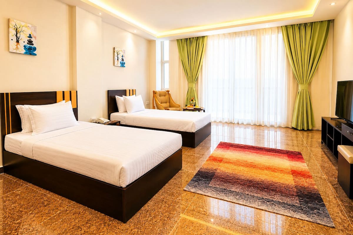 A hotel room with two beds, a TV, a desk, and a window with curtains.