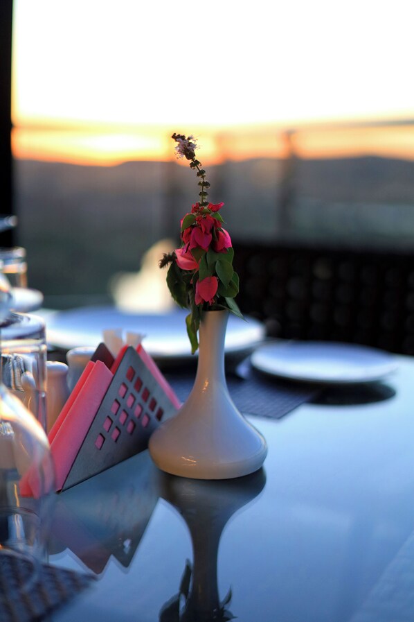 A table with a vase of flowers, a menu, and a view of the sunset. - Blue Lotus Nile Suites Hotel Aswan (Aswan)