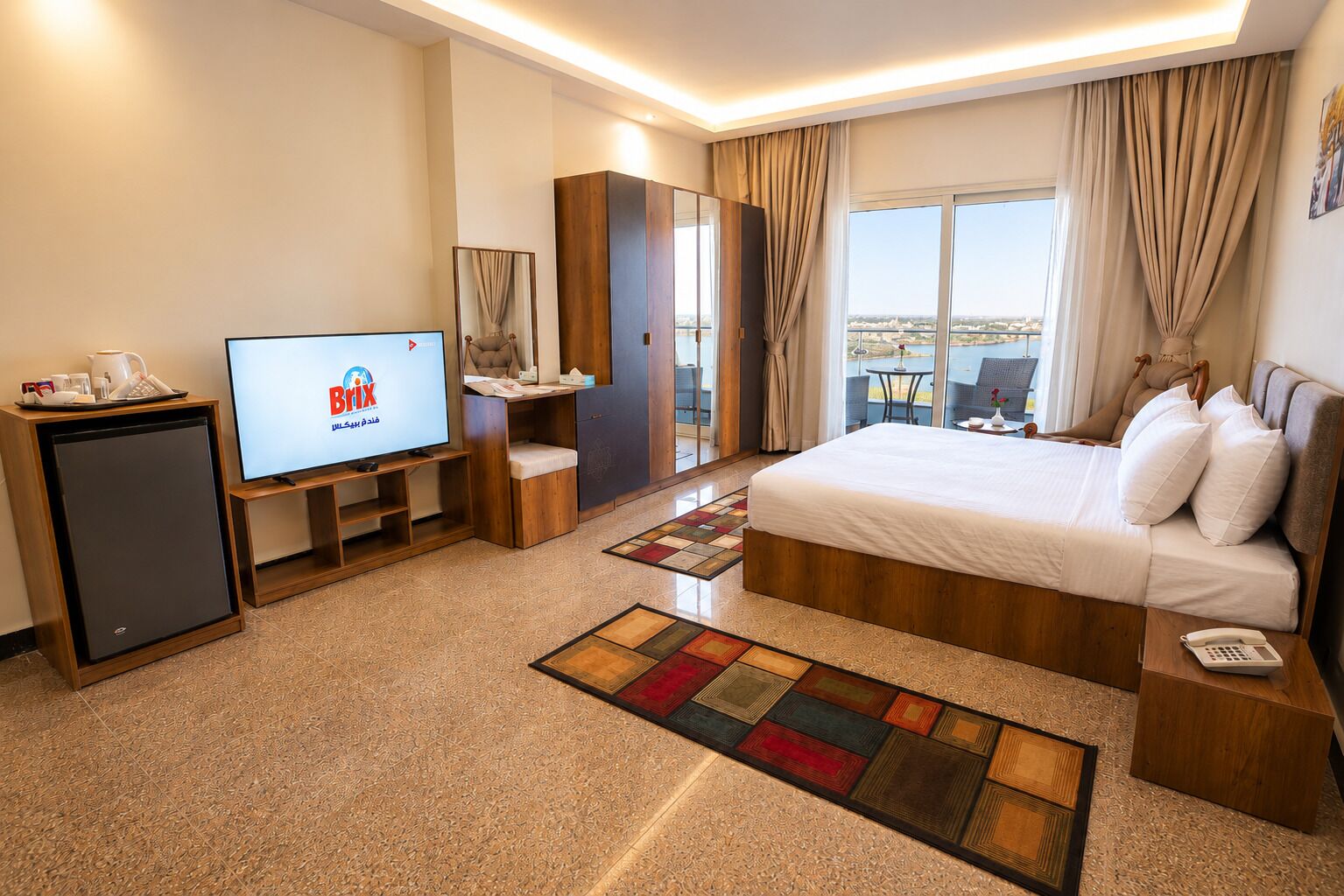 Une chambre d’hôtel équipée d’un lit, d’une télévision, d’un bureau, d’un mini-bar et offrant une vue sur la ville.