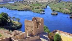 Un río con una barca, una estructura que parece un castillo y un paisaje urbano distante.