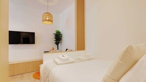 A modern hotel room with a large bed, a flat-screen TV mounted on the wall, a small plant, and neatly folded towels on a side table. - Amazing Studio - 2P - Arc de Triomphe (Paris)