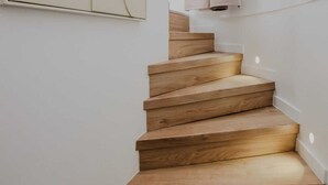 Una escalera de madera con diseño minimalista, paredes blancas y un cuadro abstracto de gran tamaño.