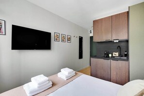 Ein modernes Hotelzimmer mit Bett, Fernseher, einer kleinen Küchenzeile und einem Wandbild.