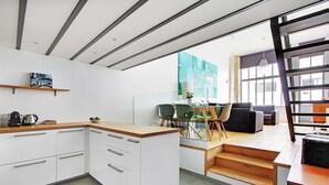 Una cocina moderna con armarios blancos, encimera de madera y una zona de comedor con sillas verdes y una mesa.