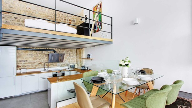 Un loft moderno con cocina, comedor y un dormitorio elevado con un muro de piedra.