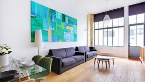 Un salón moderno con un cuadro abstracto grande, un sofá, una mesa de comedor de vidrio y un ventanal con luz natural.