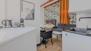 A compact hotel room with a kitchenette, a bed with a gray headboard, a gray sofa, and a dining table. - Charming Studio - 2P - Courcelles (Paris)