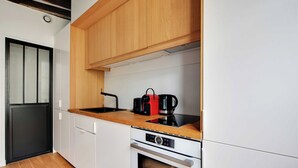 A modern kitchen with white cabinets, a wooden countertop, a Bosch oven, and a black coffee maker. - Charming Studio A/C - 2P - Le Marais (Paris)
