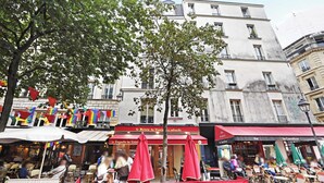 An outdoor café with tables and chairs under umbrellas, a building with a sign reading "La Baguette du Relais," and a tree in the foreground. - Charming Studio A/C - 2P - Le Marais (Paris)
