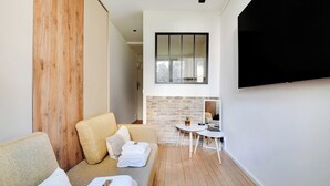 Une chambre moderne avec un mur d’accent en bois, un canapé avec des serviettes, une petite table ronde et un téléviseur fixé au mur.